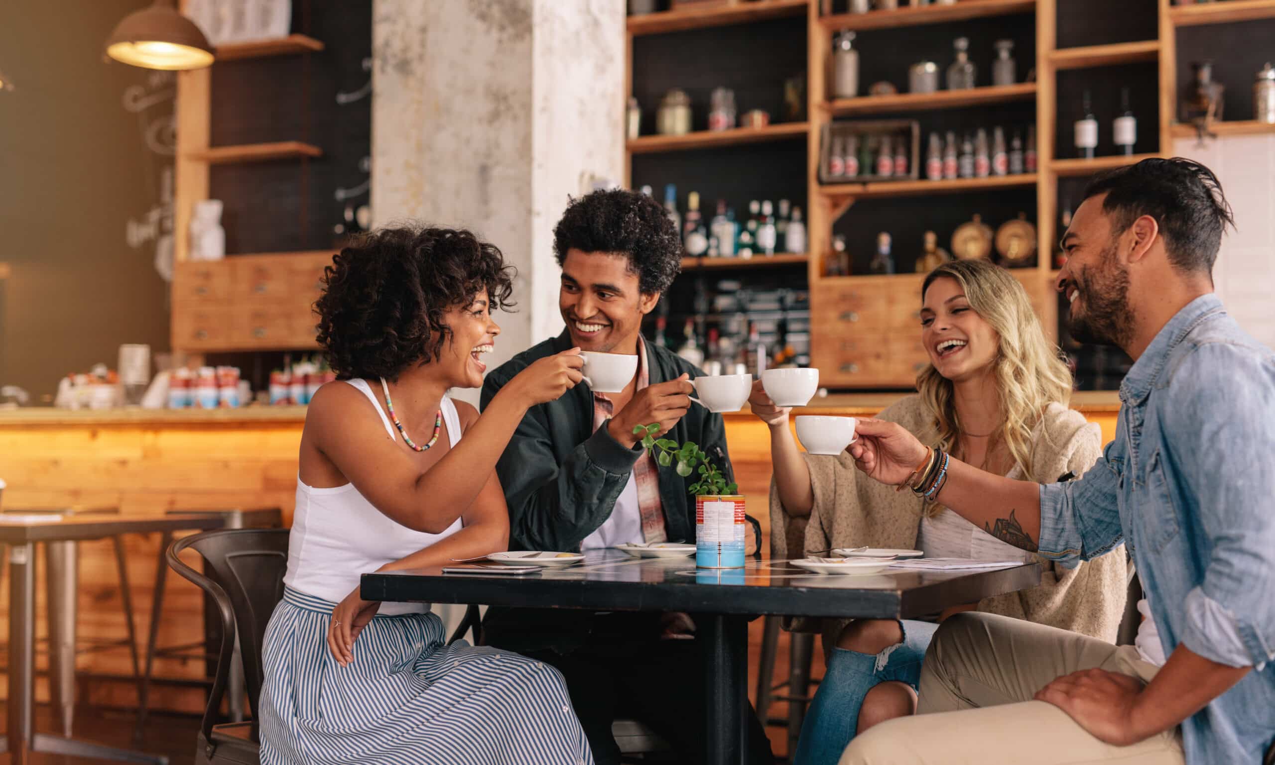 Young people sitting at cafe table and having coffee together. Group of friends making a toast with coffee.